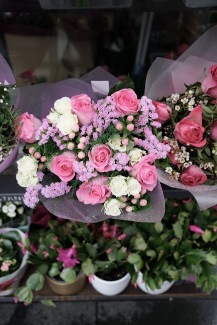 A beautifully arranged bouquet of fresh pink roses, white eustoma, and purple gypsophila flowers, wrapped in delicate lavender tissue paper and tied with a soft pink ribbon. The bouquet is displayed o
